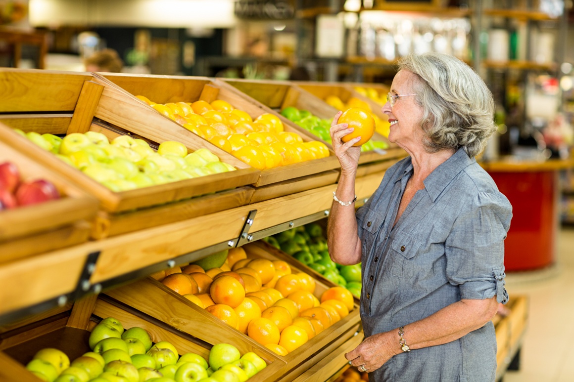 Older woman standing in front of a fruit shelf in the supermarket and smelling...