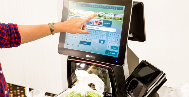 Photo: Person operating a self-checkout terminal; copyright: NCR GmbH...