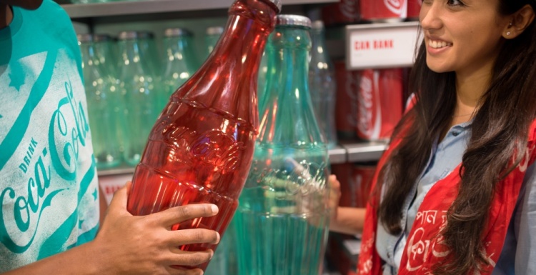 Two people holding big colored coca cola bottles; copyright: The Coca-Cola...