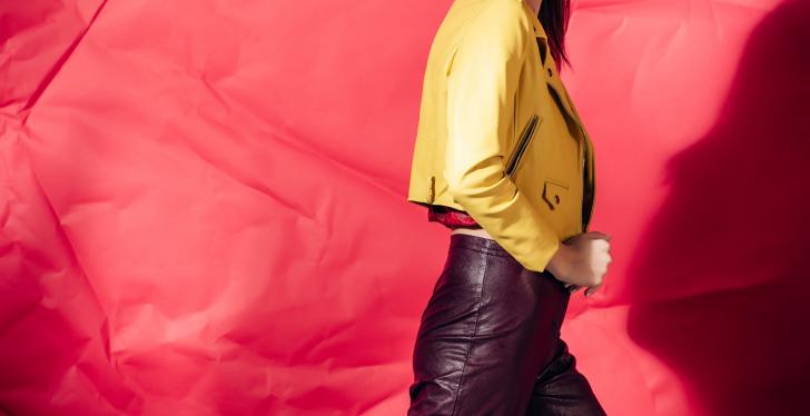 Woman wearing and showcasing a yellow leather jacket in front of a red...