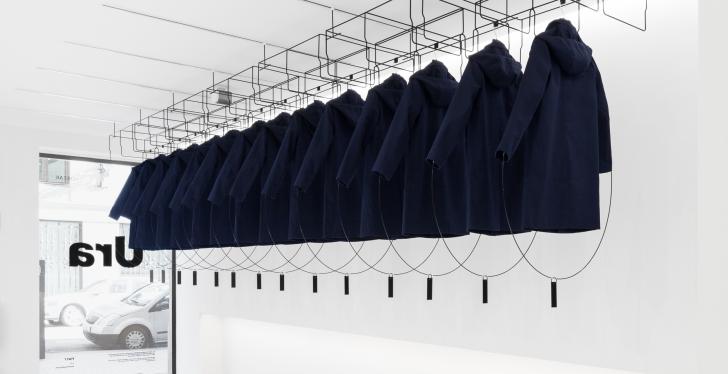 Installation in an empty white store with rain coats hanging from the ceiling;...
