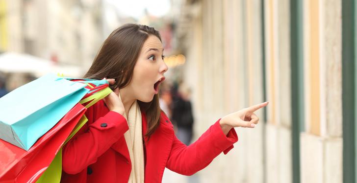 Amazed female customer with shopping bags staring and pointing into a shop...