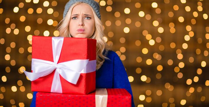 Woman looking unhappy, holding to big wrapped gift boxes under her chin with...