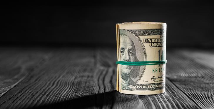 A roll of dollar bills standing on a wooden table