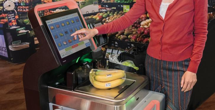 A woman is standing at a self-service checkout in the supermarket and typing on...