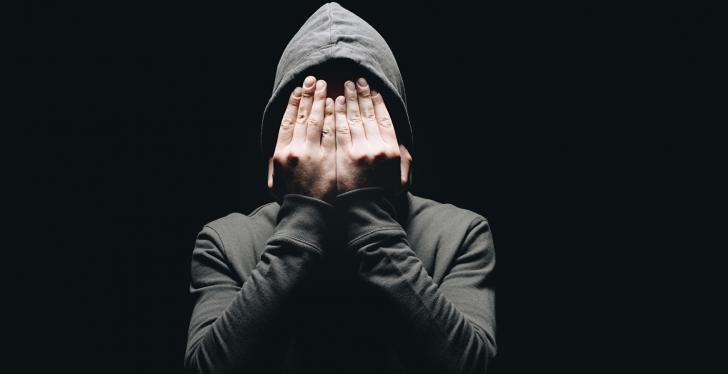 A person in a hoodie puts his hands in front of his face...