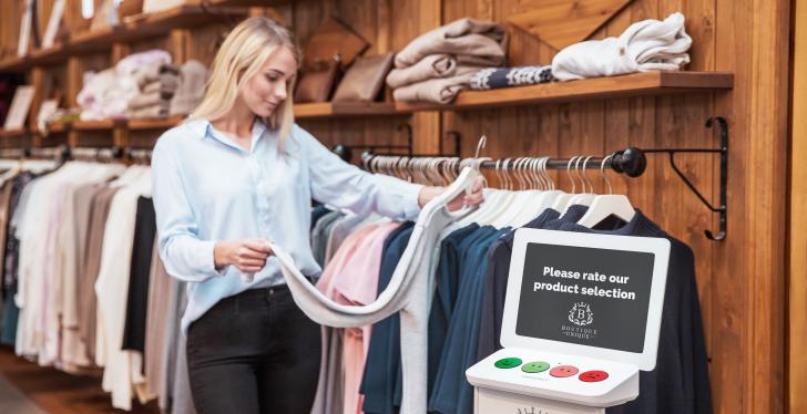 A woman in a clothing shop; in front of her a terminal where she can indicate...