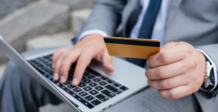 A man holding a laptop on his knees and a card in his hand...