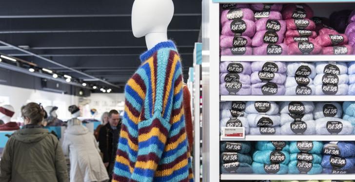 A mannequin with sweater next to a shelf with wool