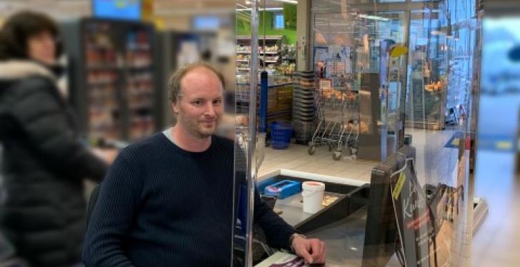 Employees of a supermarket sitting at the cash register behind a spit...