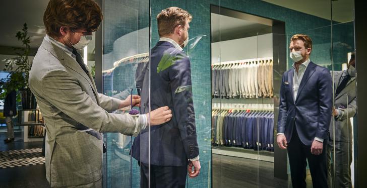 A tailor works on a suit a man inside a glass box is wearing...