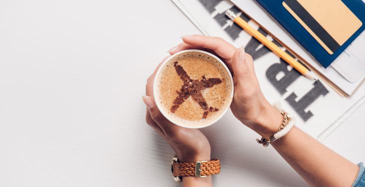 Woman holding a cup of capuccino with an airplane drawn in...