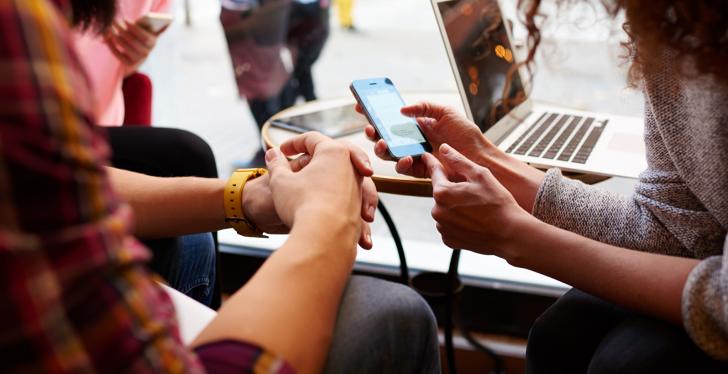 Two women sitting at a table. One of them is holding a smartphone...