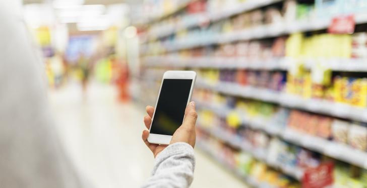 Person in front of a supermarket shelf holding a smartphone...