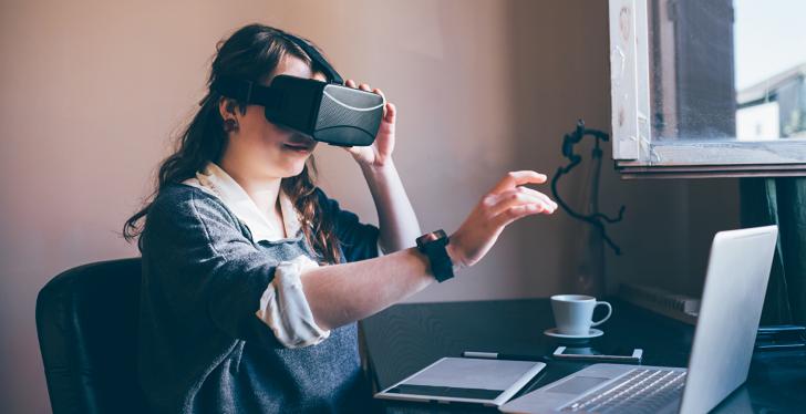 A woman wearing a VR headset in front of her laptop...