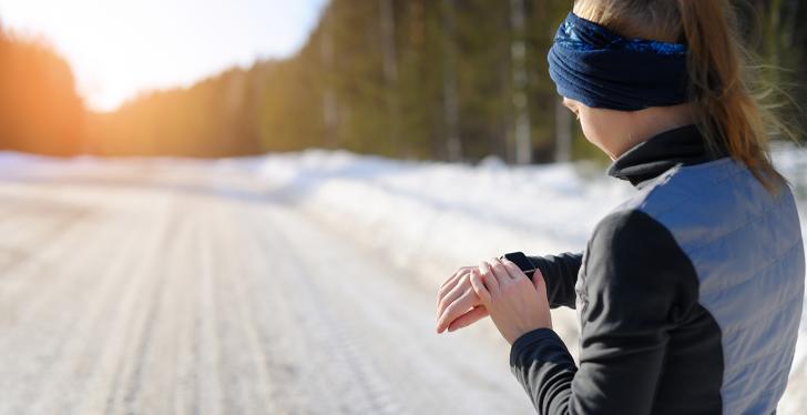 A woman in sportswear stands on a snow covered road and looks at her Smart Watch...