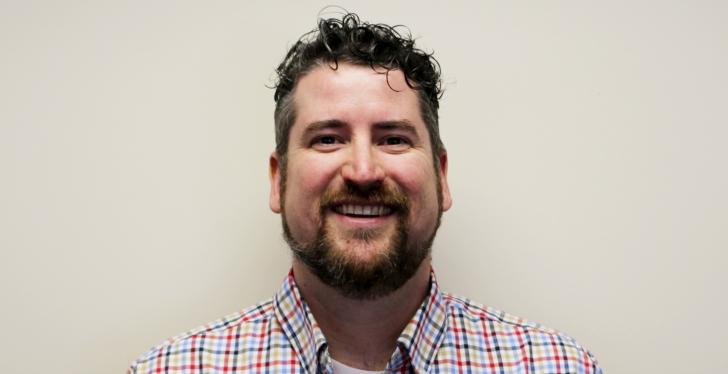 A man in a plaid shirt smiling into the camera