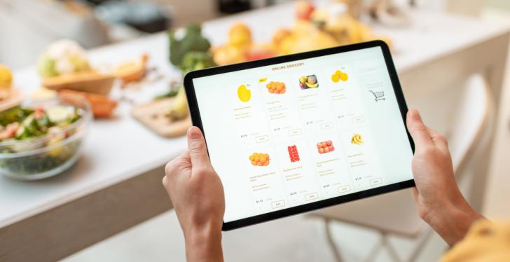 A person is shopping groceries online with a tablet, in front of a table with...
