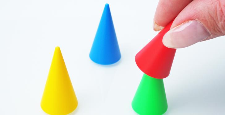 A hand puts a green playing cone over a red