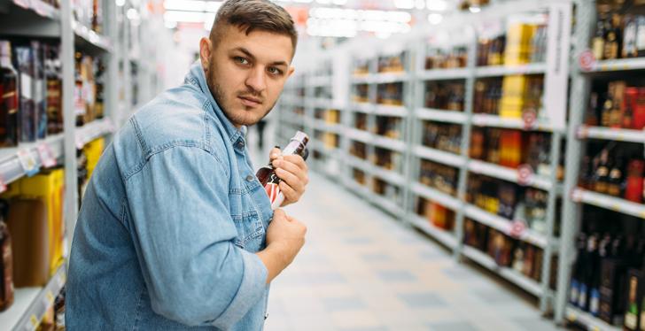 A man is sticking a bottle into his shirt in a store...