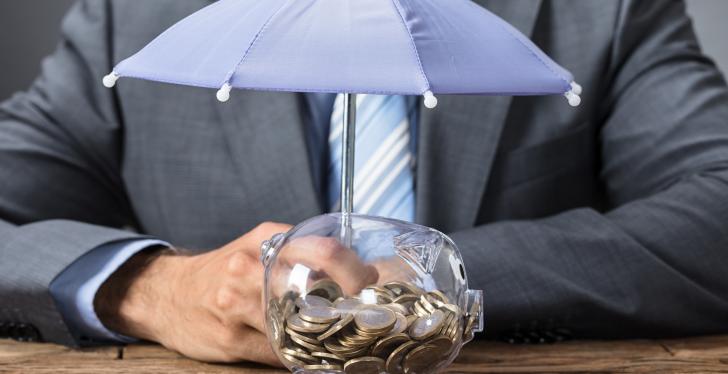 A business man sitting behind a piggybank with a small umbrella over it...