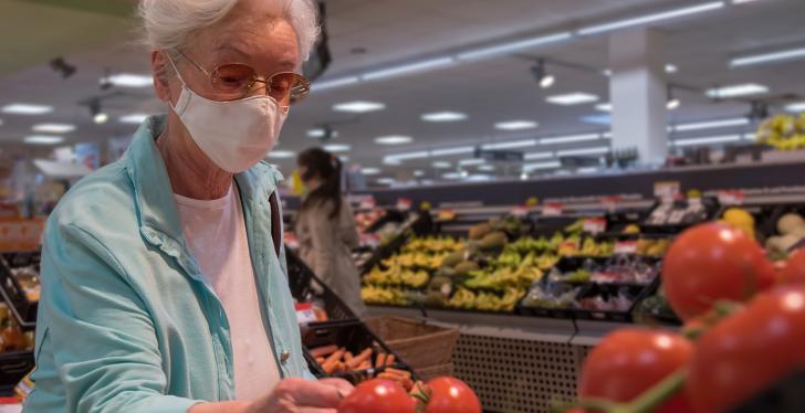 An elderly woman is looking at tomatoes in a supermarket, wearing a face mask...