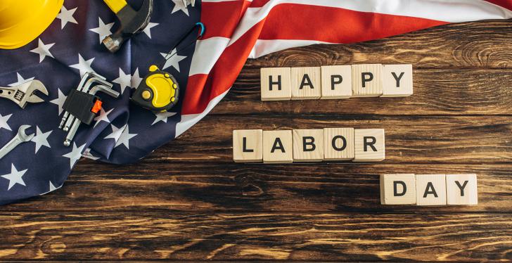 An American flag and tools lying on a wooden table with blocks spelling Happy...