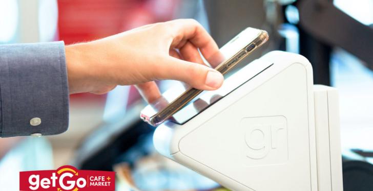 A hand holding a smartphone to a checkout device