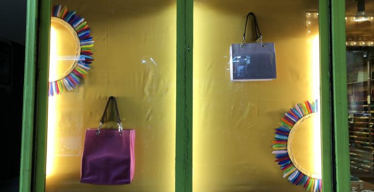 An illuminated shop window with a yellow background and two handbags and...