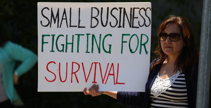 A woman holding a sign that says “small businesses fighting for survival”;...