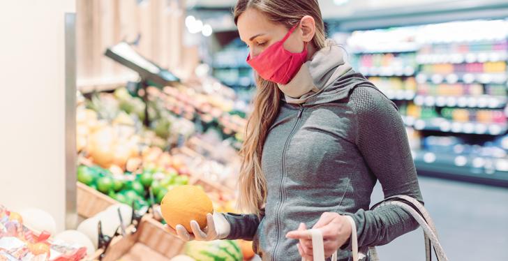 A woman is standing in a supermarket holding an orange...