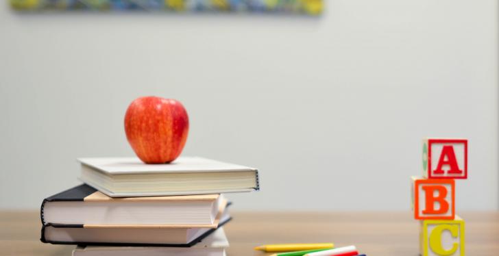 An apple lays on a pile of books next to pencils and colorful dices with letters...