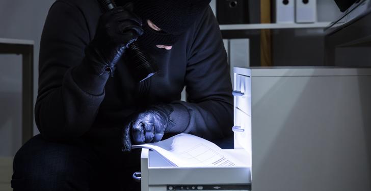 thief with flashlight looks into a drawer