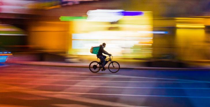 Person on a bicycle in front of a blurred city backdrop; Source: Paolo...