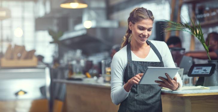 An employee in a catering business operates a tablet PC while leaning against...