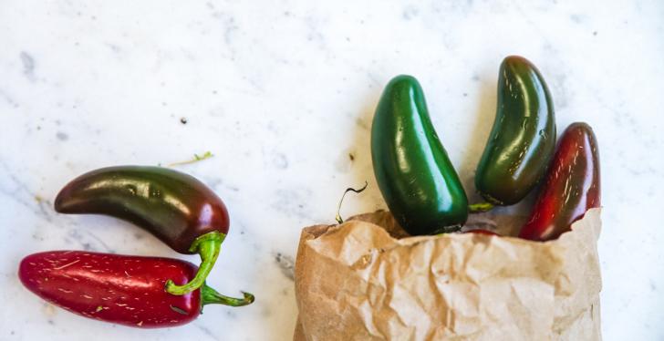 Green and red chili peppers fall out of a paper bag onto a table; copyright:...