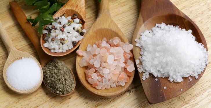 Several wooden spoons of different sizes filled with different shapes of salt...