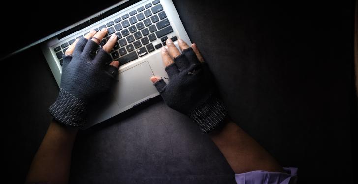 A person using a laptop in the dark while wearing fingerless gloves....