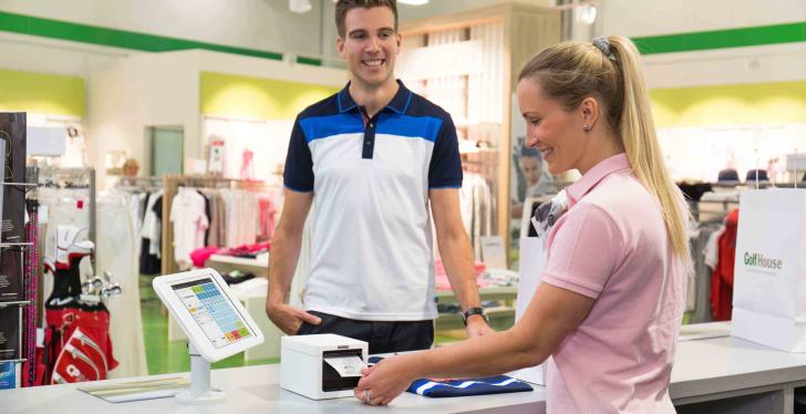 A smiling cashier takes a receipt from a checkout printer, with a smiling...