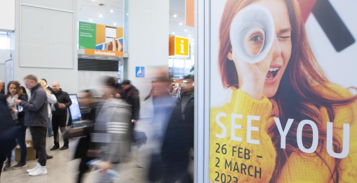 A poster at EuroShop 2020 announces EuroShop 2023. Visitors walk behind it....