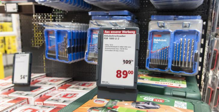 An electronic price tag in front of a shelf with drills in a hardware store;...
