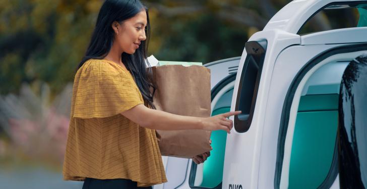 A person is taking a bag with groceries out of an autonomous vehicle by Nuro...