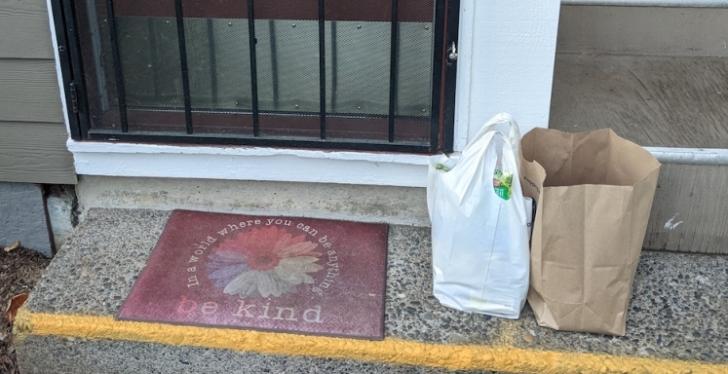 The front porch of an apartment with a welcome mat saying Be Kind and two bags...