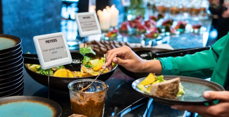 A person takes something from a buffet. Two digital buffet signs can be seen....