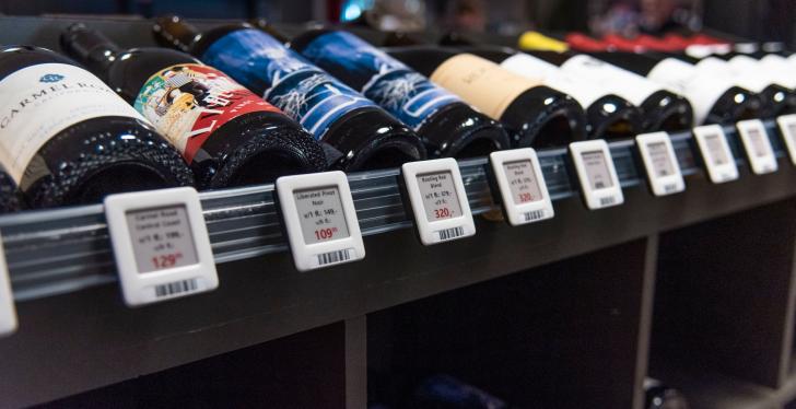 Various wine bottles lie on a shelf. Electronic shelf labels are attached to...
