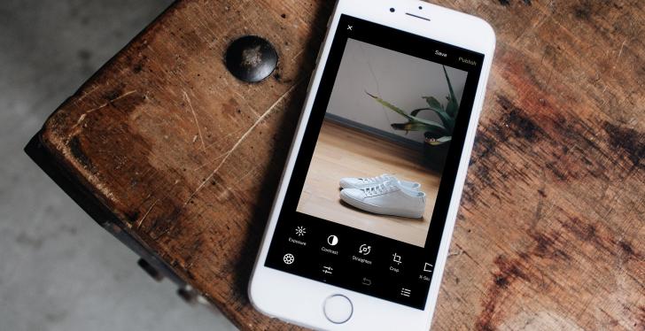 A cell phone on a wooden table with a picture of white shoes on it...