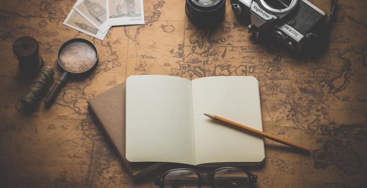 On a card table there is a notebook with a pen, a magnifying glass and a camera...