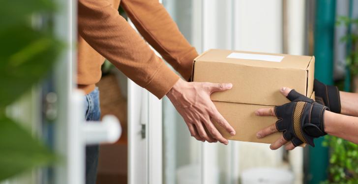 A person hands over a parcel to another person at the front door...