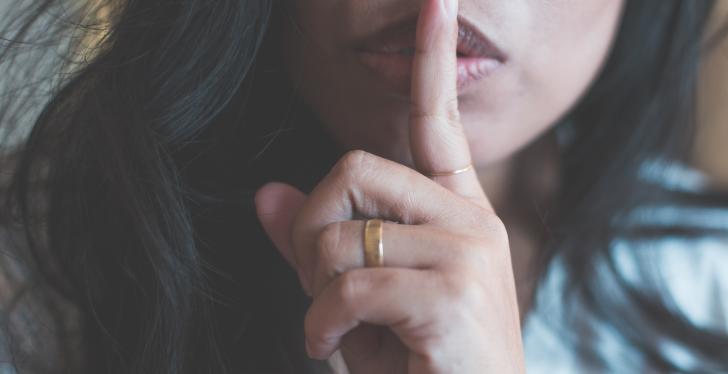A woman holds her index finger to her lips