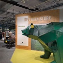 A green metal bear stands in front of a wooden wall with the inscription...